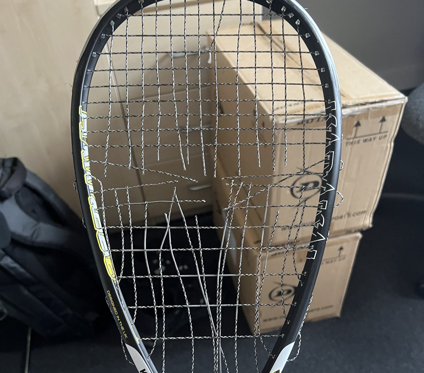 Squash racket with frayed, snapped strings that need replacing