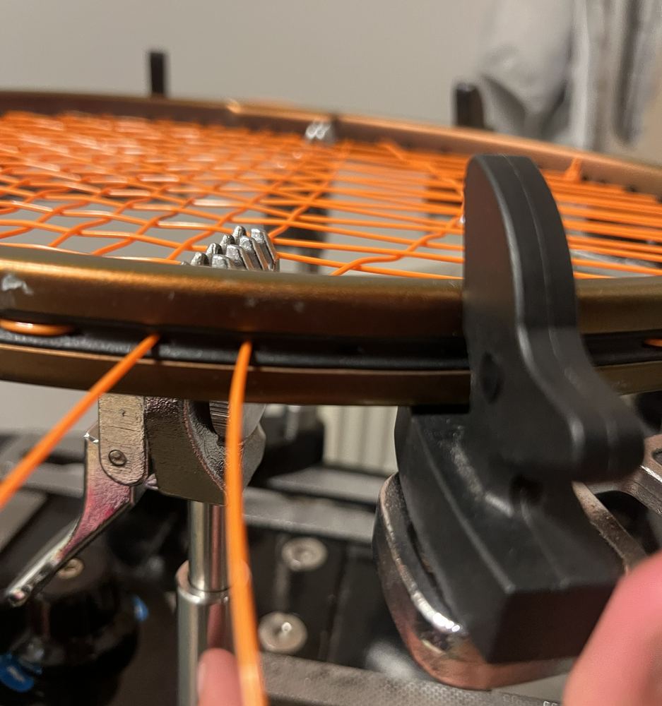 Orange string being pulled through the clamp on the stringing machine