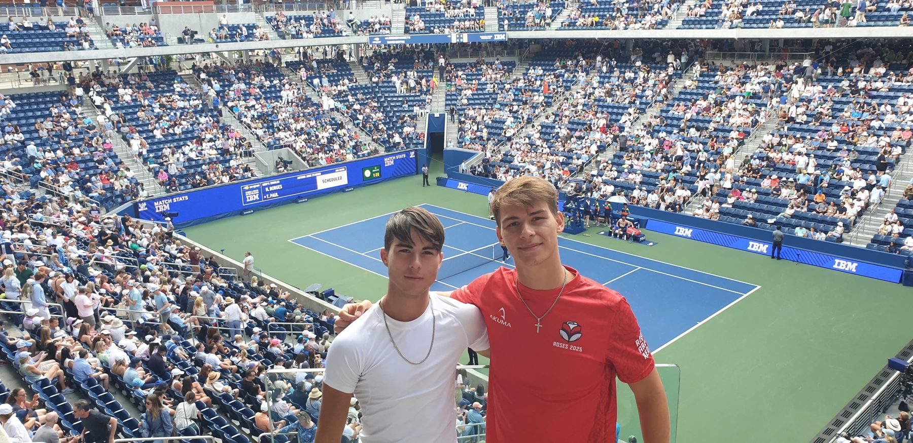 Luka and Matty Matellini side by side in the stands at the US Open, with the court behind them